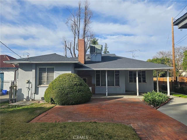 rear view of house with a lawn, a chimney, fence, central air condition unit, and stucco siding