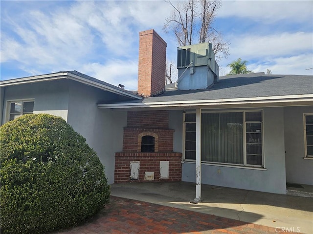 exterior space with brick siding, a chimney, central AC, and stucco siding