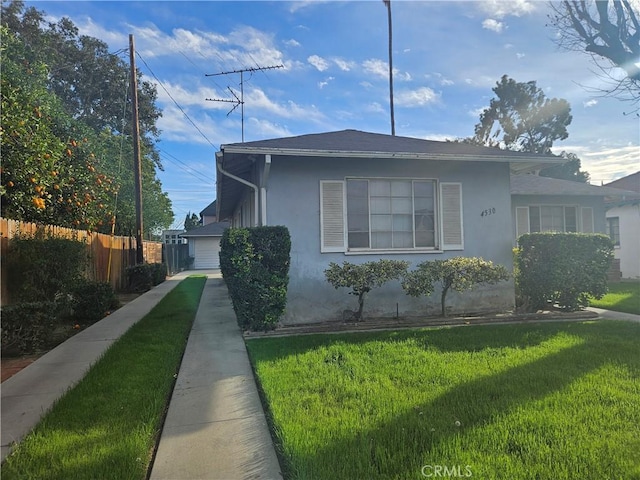 view of side of home featuring fence, a lawn, and stucco siding