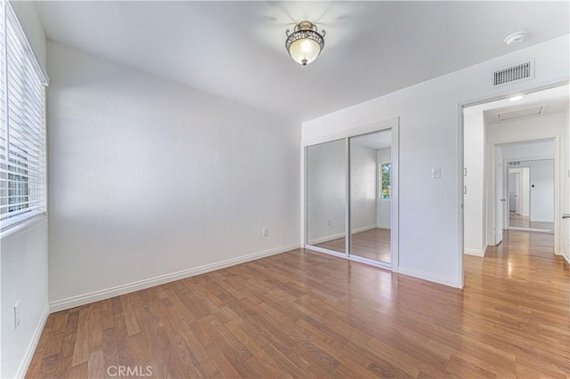 unfurnished bedroom featuring baseboards, a closet, visible vents, and wood finished floors