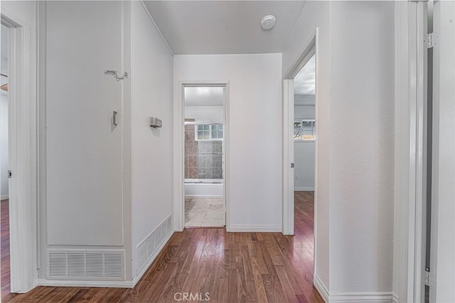 hallway with baseboards, visible vents, and wood finished floors