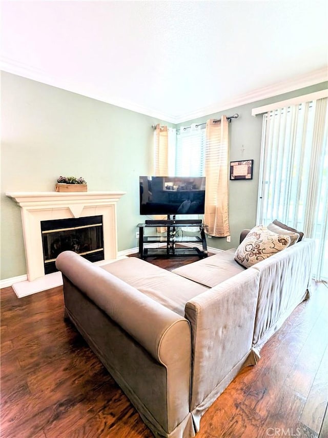 living area featuring baseboards, wood finished floors, a glass covered fireplace, and crown molding