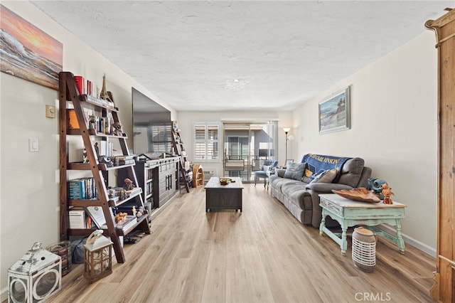 living area with light wood-type flooring, a textured ceiling, and baseboards