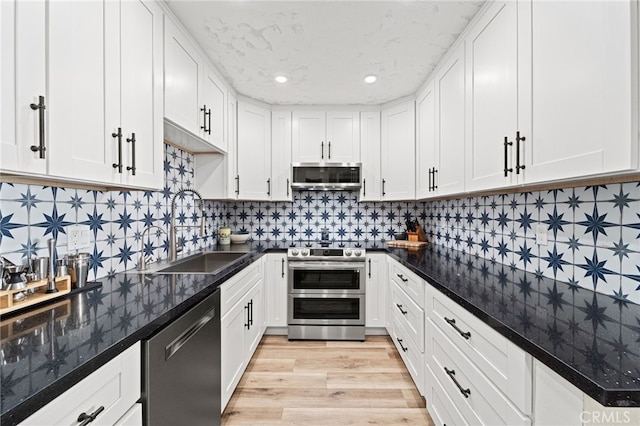 kitchen with stainless steel appliances, light wood-style floors, white cabinets, a sink, and extractor fan