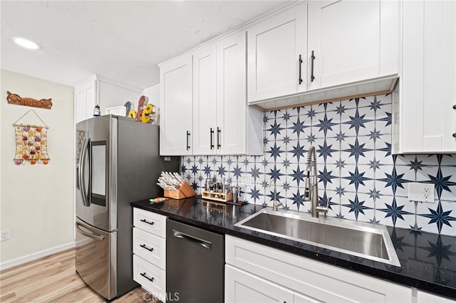 kitchen with light wood finished floors, stainless steel appliances, backsplash, white cabinetry, and a sink