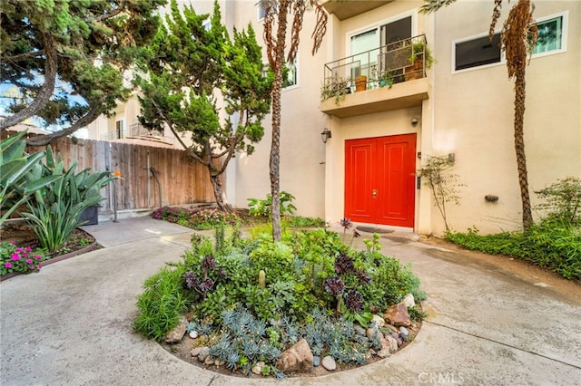 view of exterior entry with fence, a balcony, and stucco siding