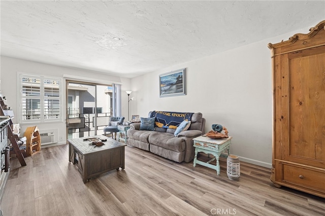 living room featuring baseboards, a wall unit AC, light wood-style flooring, and a textured ceiling