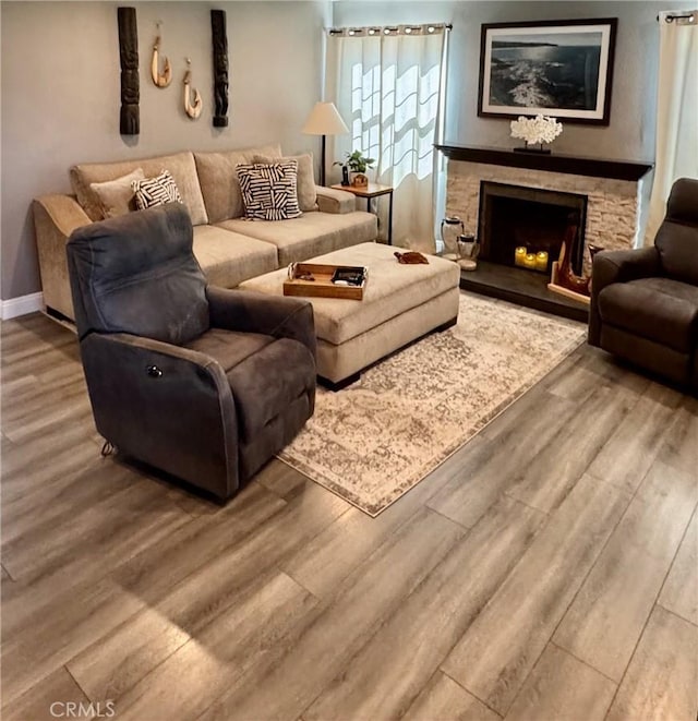 living area featuring a stone fireplace, baseboards, and wood finished floors