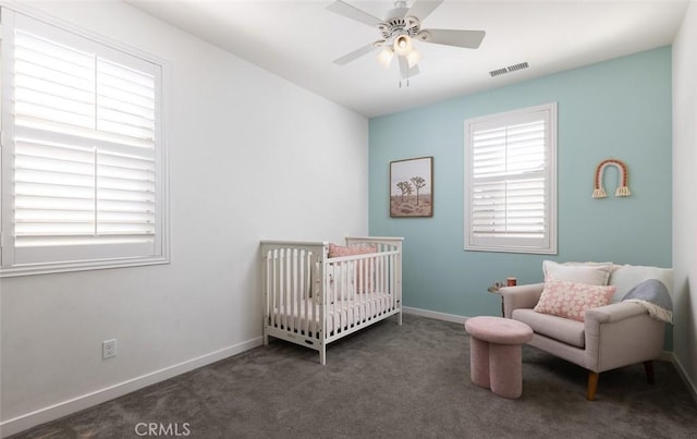 carpeted bedroom with visible vents, baseboards, a crib, and a ceiling fan