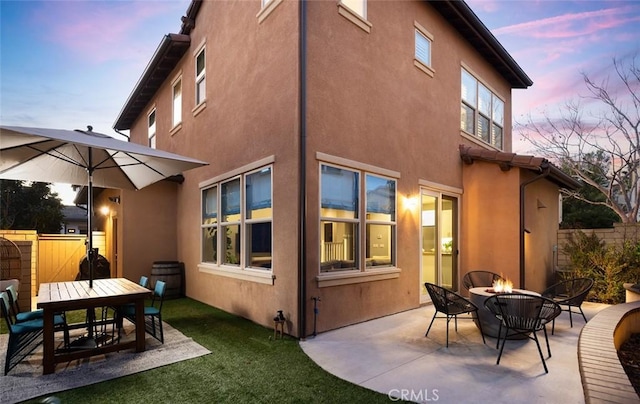 back of house at dusk with stucco siding, a patio, fence, and an outdoor fire pit