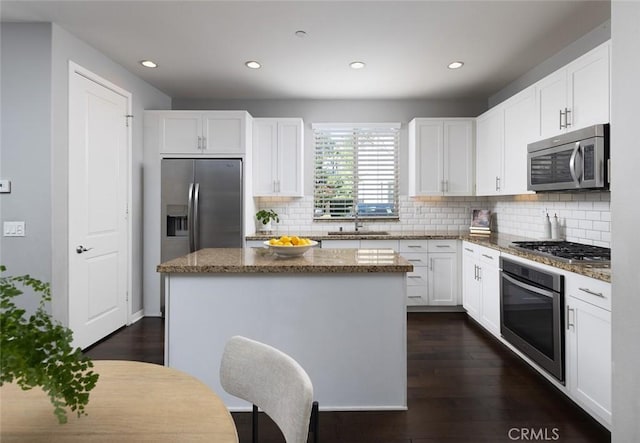 kitchen with stone counters, dark wood finished floors, a sink, stainless steel appliances, and a center island