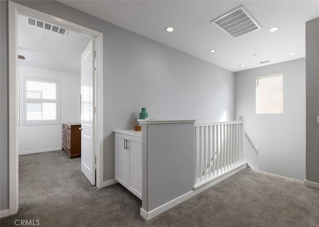 hallway featuring dark colored carpet, visible vents, and an upstairs landing