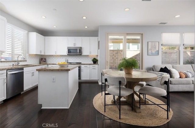 kitchen with a sink, light stone counters, backsplash, a center island, and appliances with stainless steel finishes