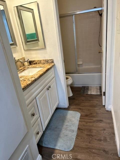 bathroom featuring toilet, combined bath / shower with glass door, wood finished floors, and vanity