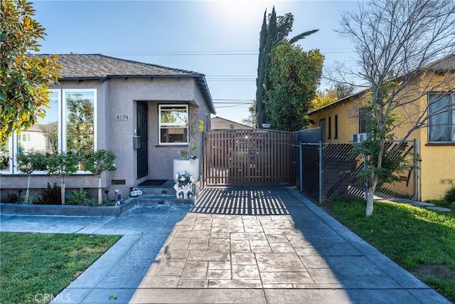 exterior space featuring a gate, fence, roof with shingles, and stucco siding