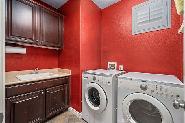 laundry area with cabinet space, washer and clothes dryer, a sink, and a textured wall