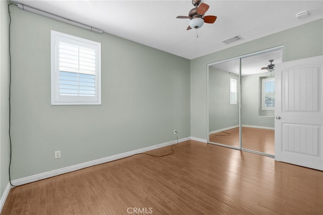 unfurnished bedroom featuring ceiling fan, wood finished floors, visible vents, baseboards, and a closet