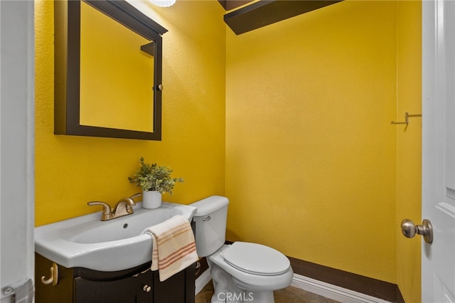 half bathroom with vanity, toilet, and baseboards