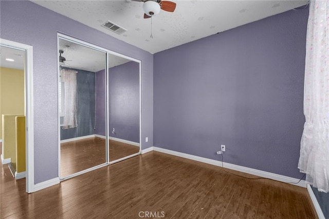 unfurnished bedroom with a closet, wood finished floors, visible vents, and baseboards