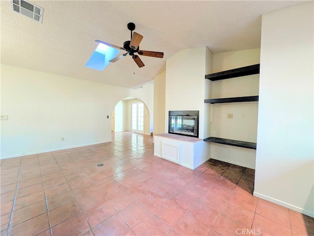 unfurnished living room with arched walkways, vaulted ceiling with skylight, a textured ceiling, visible vents, and a ceiling fan