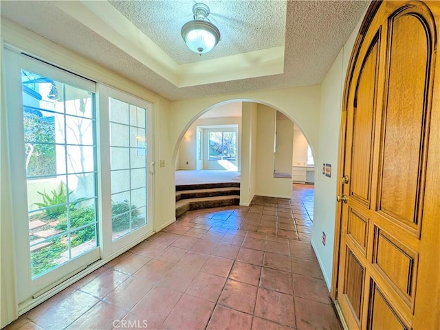 doorway to outside with arched walkways, a textured ceiling, baseboards, and light tile patterned floors