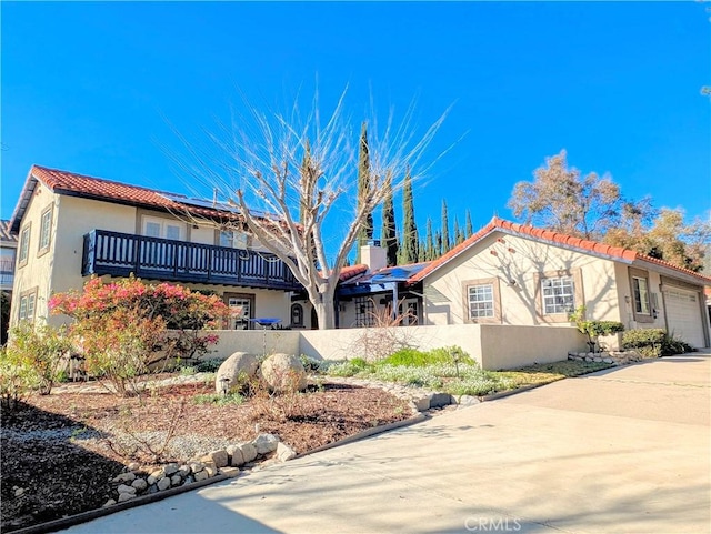 mediterranean / spanish-style home featuring a fenced front yard, an attached garage, concrete driveway, roof mounted solar panels, and stucco siding