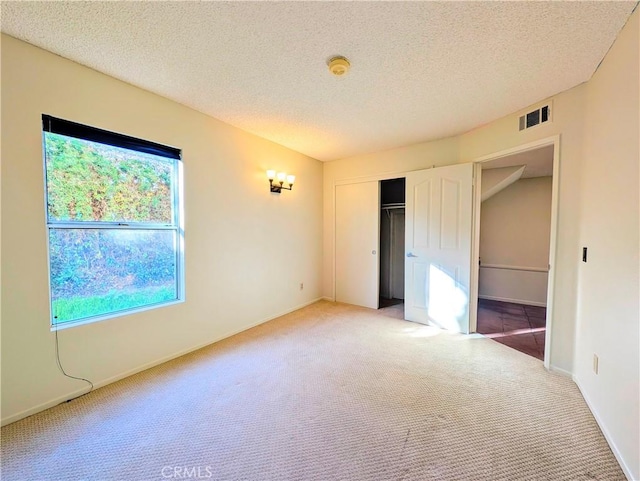 unfurnished bedroom with a textured ceiling, carpet floors, a closet, and visible vents