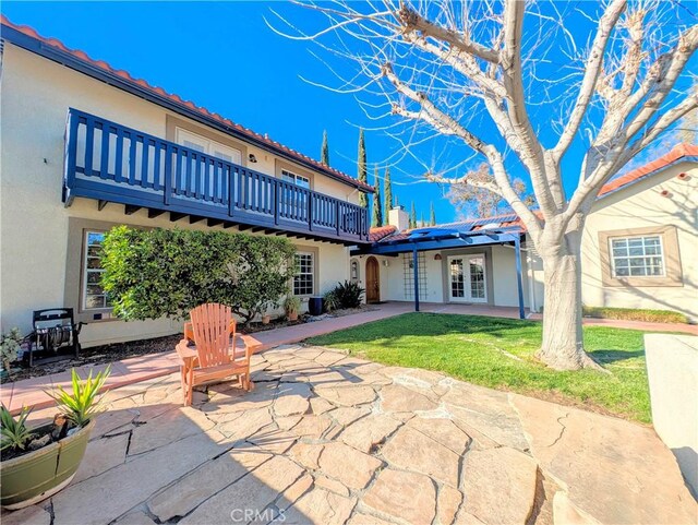 rear view of house featuring stucco siding, a patio area, a lawn, and french doors