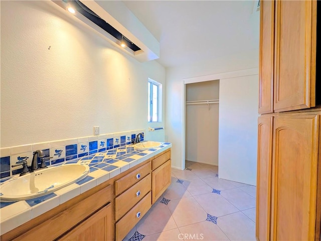 full bathroom with a walk in closet, double vanity, a sink, and tile patterned floors