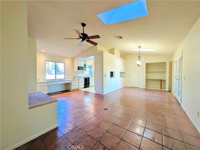 unfurnished living room featuring lofted ceiling with skylight, ceiling fan, visible vents, and a textured ceiling