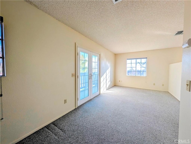 empty room with a textured ceiling, french doors, carpet flooring, and visible vents