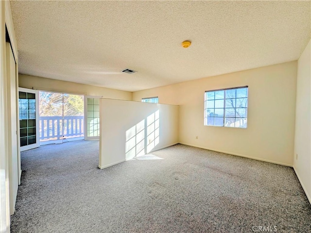 carpeted spare room featuring plenty of natural light, visible vents, and baseboards