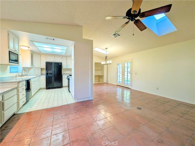 kitchen featuring vaulted ceiling with skylight, visible vents, light countertops, built in microwave, and black refrigerator with ice dispenser