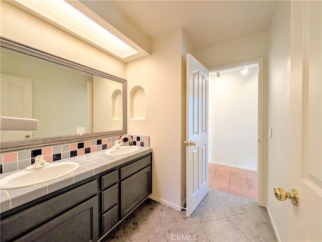 full bath featuring double vanity, backsplash, a sink, and baseboards