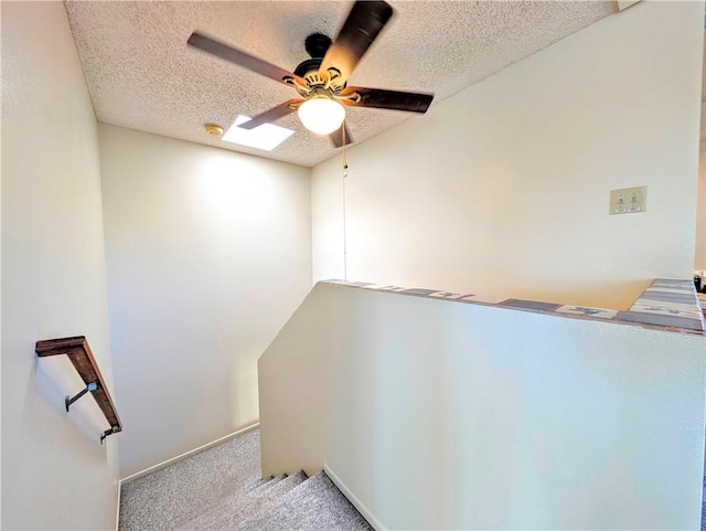 interior space featuring a skylight, baseboards, a ceiling fan, a textured ceiling, and carpet floors