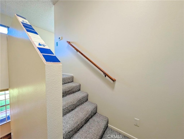 stairway featuring carpet floors, baseboards, and a textured ceiling