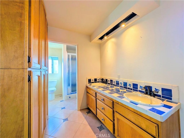 bathroom with double vanity, toilet, a sink, a shower stall, and tile patterned flooring