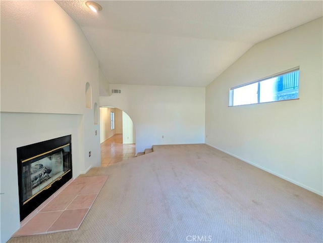 unfurnished living room featuring arched walkways, carpet, a fireplace, lofted ceiling, and visible vents