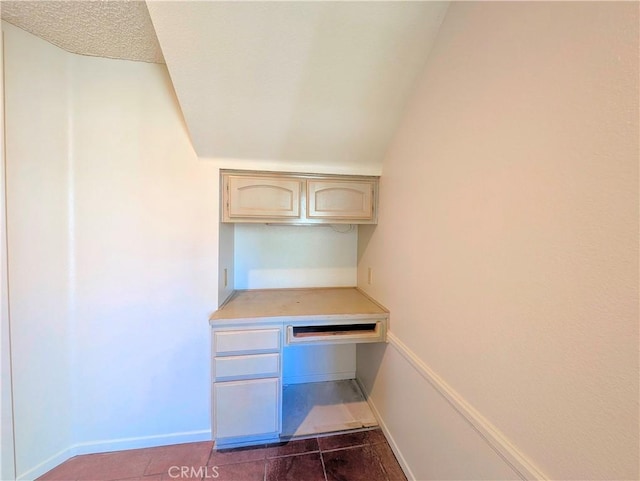 unfurnished office featuring dark tile patterned floors, baseboards, and built in desk