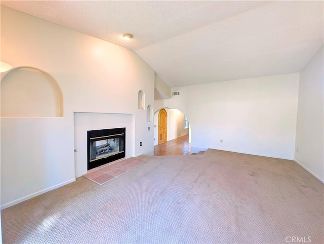 unfurnished living room with lofted ceiling, arched walkways, carpet flooring, and a tile fireplace