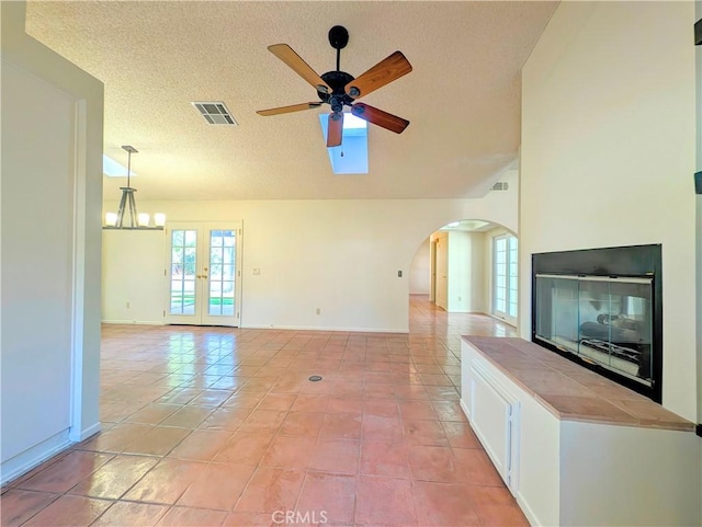 unfurnished living room with visible vents, arched walkways, a glass covered fireplace, a textured ceiling, and ceiling fan with notable chandelier