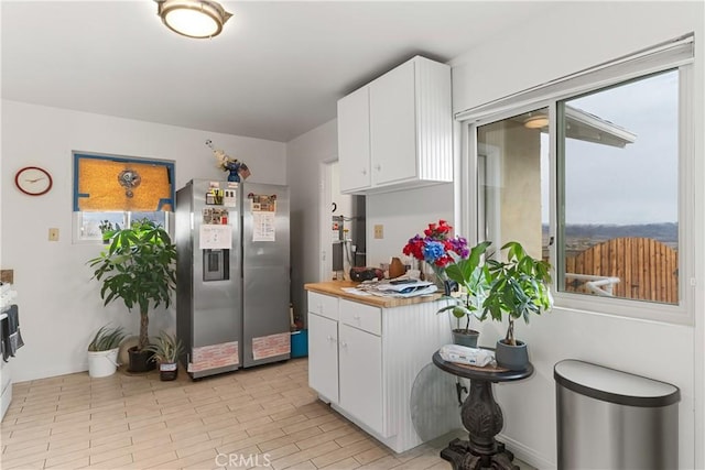 kitchen featuring plenty of natural light, stainless steel fridge, white cabinetry, and light countertops