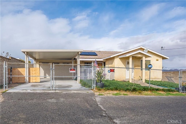 view of front facade with an attached carport, a gate, stucco siding, a fenced front yard, and roof mounted solar panels