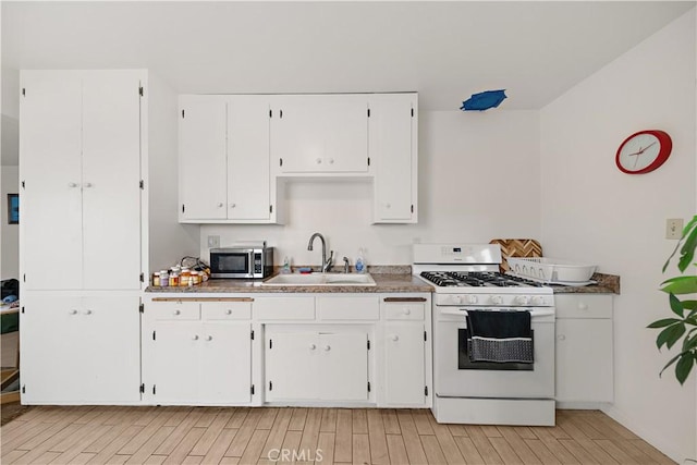 kitchen featuring wood finish floors, white gas stove, a sink, stainless steel microwave, and white cabinets