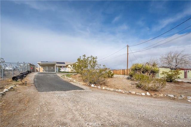 view of front of house with a gate, roof mounted solar panels, dirt driveway, and fence