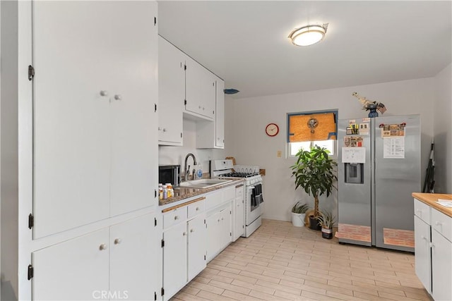 kitchen with white gas stove, light wood-type flooring, white cabinets, stainless steel fridge, and a sink