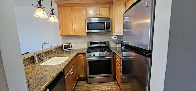 kitchen with stainless steel appliances, tasteful backsplash, hanging light fixtures, a sink, and dark stone counters