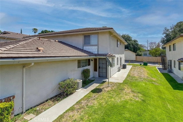 exterior space featuring a tiled roof, fence, a front lawn, central AC, and stucco siding