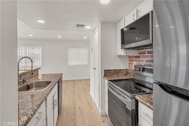 kitchen with tasteful backsplash, appliances with stainless steel finishes, light wood-style floors, white cabinetry, and a sink