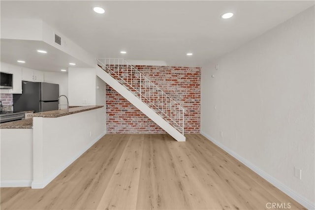 living area featuring light wood-style flooring, recessed lighting, brick wall, baseboards, and stairs